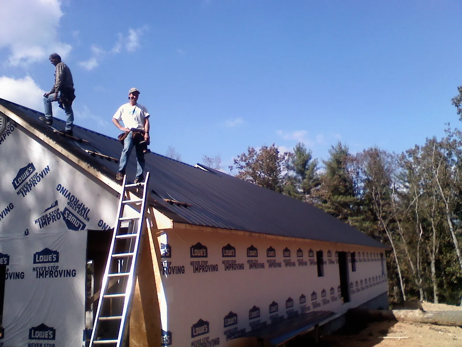 Two roofers standing on a long dark metal roof over a wrapped building in Lincoln