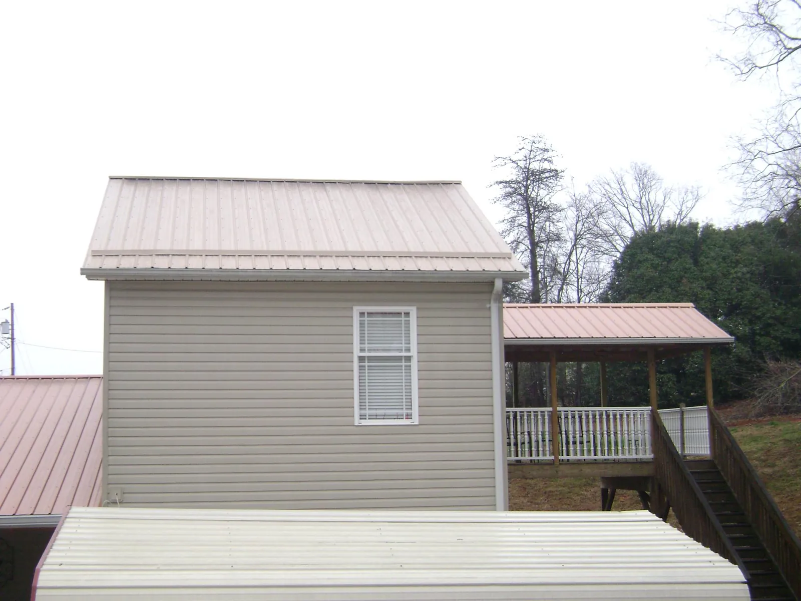 Tan metal roofs on a two story addition and attached porch, from a Roof Replacement job in Lincoln